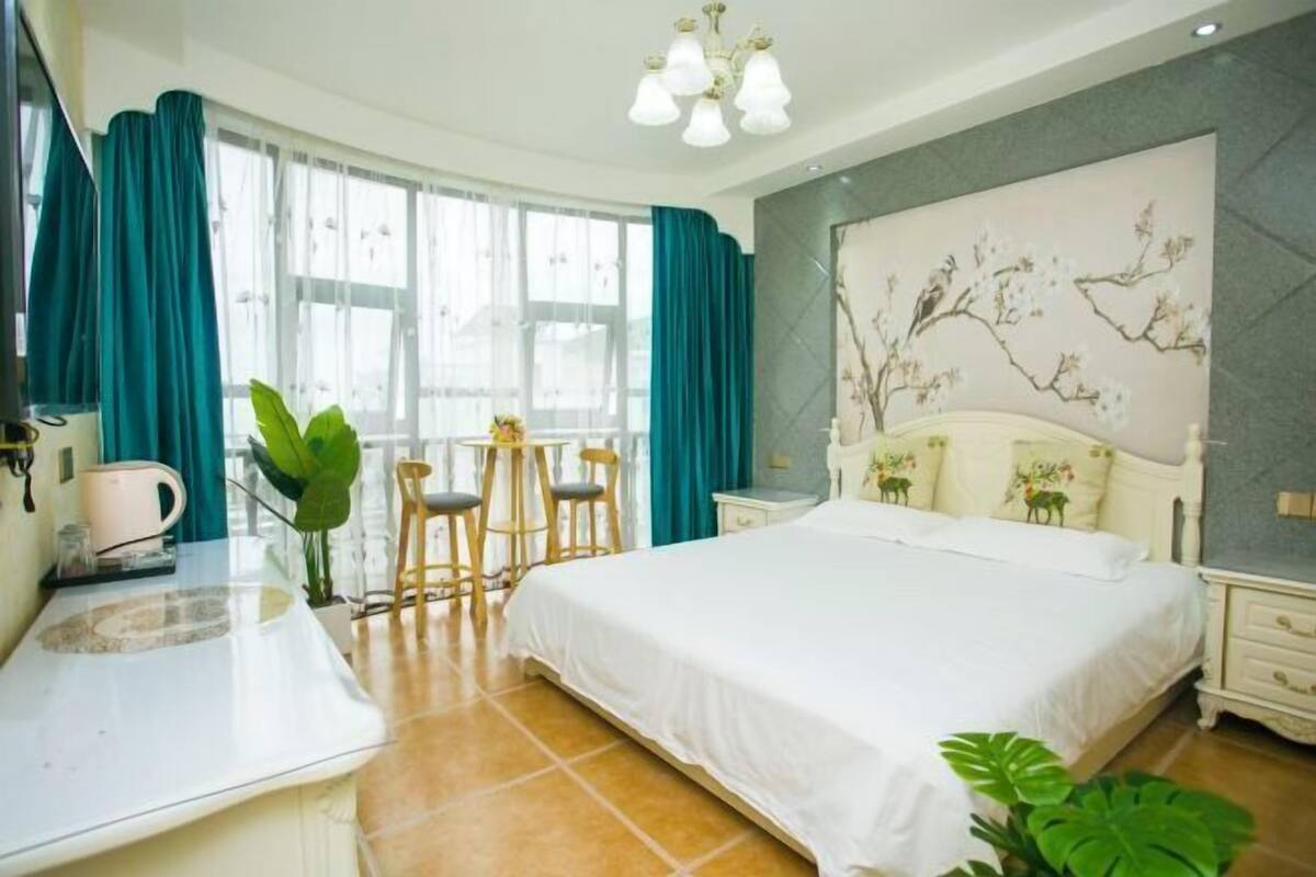 Une chambre d’hôtel comprenant un lit, un bureau avec une chaise, une machine à café et une grande fenêtre avec des rideaux.