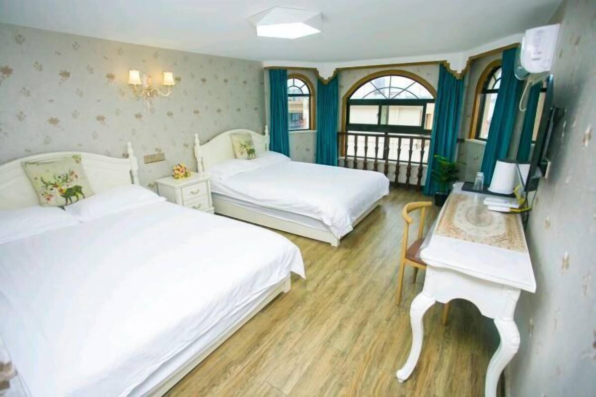 Une chambre d’hôtel avec deux lits simples, une petite table de chevet avec une lampe, une chaise et une grande fenêtre avec des rideaux.
