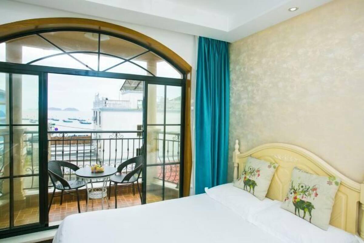 Une chambre d’hôtel avec un lit, un balcon avec des chaises et une vue sur la mer.