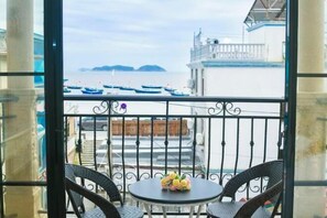 A balcony with wicker chairs and a small table with flowers, overlooking a marina with boats and buildings.