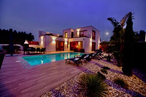 A modern two-story house with a swimming pool, lounge chairs, and a well-lit outdoor area. - Villa Serena - Exquisite Villa in São Martinho do Porto with Heated Private Pool (São Martinho do Porto)