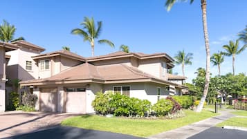 A two-story residential house with a garage, surrounded by well-maintained lawns and palm trees.