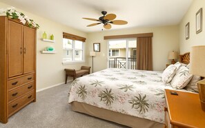 A bedroom with a bed, a wooden wardrobe, a chair, a desk, a ceiling fan, a window, and a balcony.