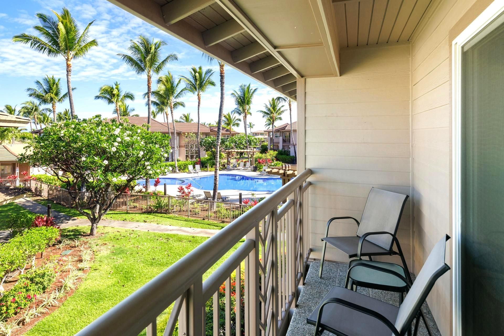 A balcony with a pool view, chairs, and a garden.
