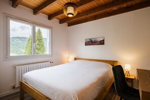 A bedroom with a wooden bed, a radiator, a window with a view of trees, and a painting on the wall.