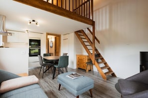 Ein modernes Wohnzimmer mit einer Holztreppe, einem Essbereich mit Tisch und Stühlen sowie einer Küche mit eingebautem Ofen.