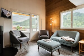 A modern living room with a sofa, two armchairs, a coffee table, and a fireplace. Large windows offer views of a mountainous landscape.