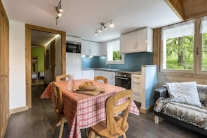 Uma cozinha acolhedora com uma mesa de jantar posta para dois, geladeira e uma janela com vista para o verde.