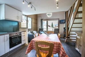 A kitchen with a stove, oven, and dining area with a checkered tablecloth. - 1st floor, view mountain, balcony, fireplace or stove, tv, ski locker, 55m², La Clusaz (La Clusaz)