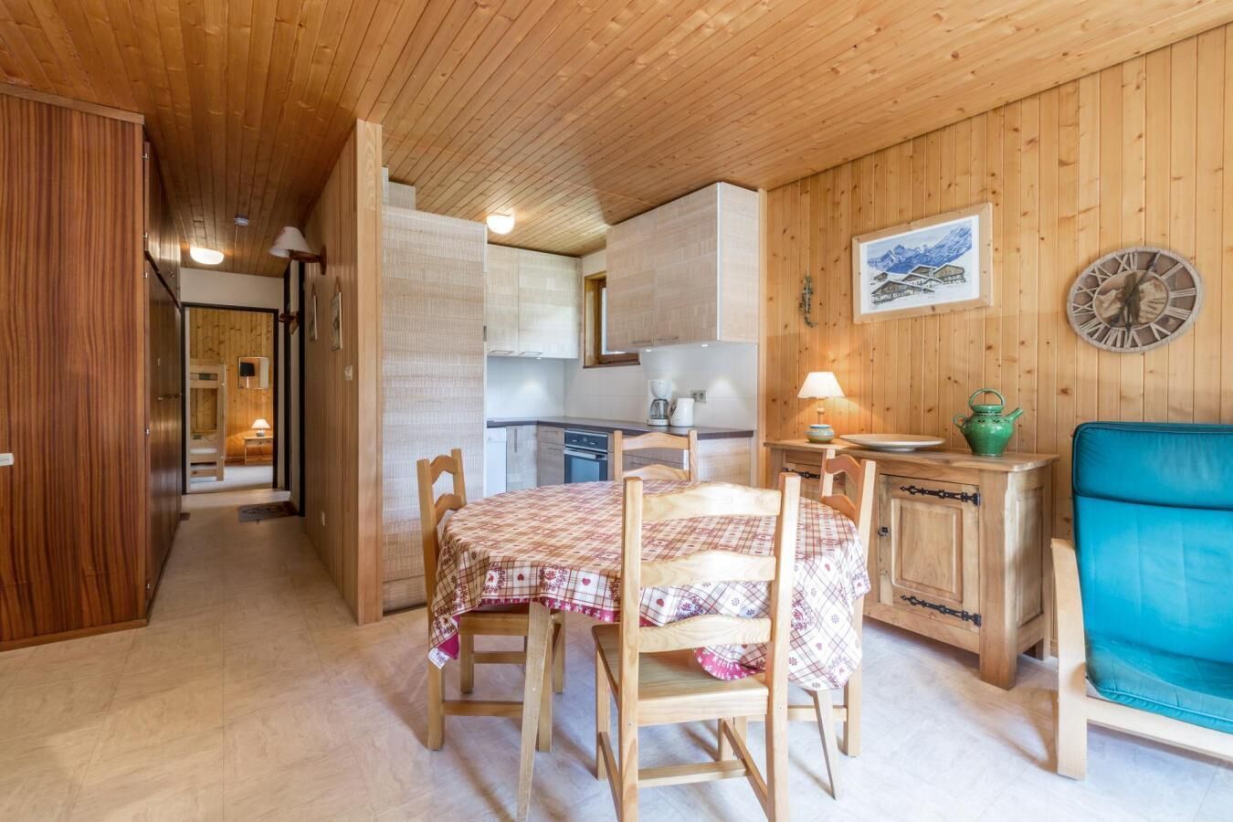 Un interior de madera con una mesa de comedor preparada para cuatro personas, una zona de cocina y una silla azul.
