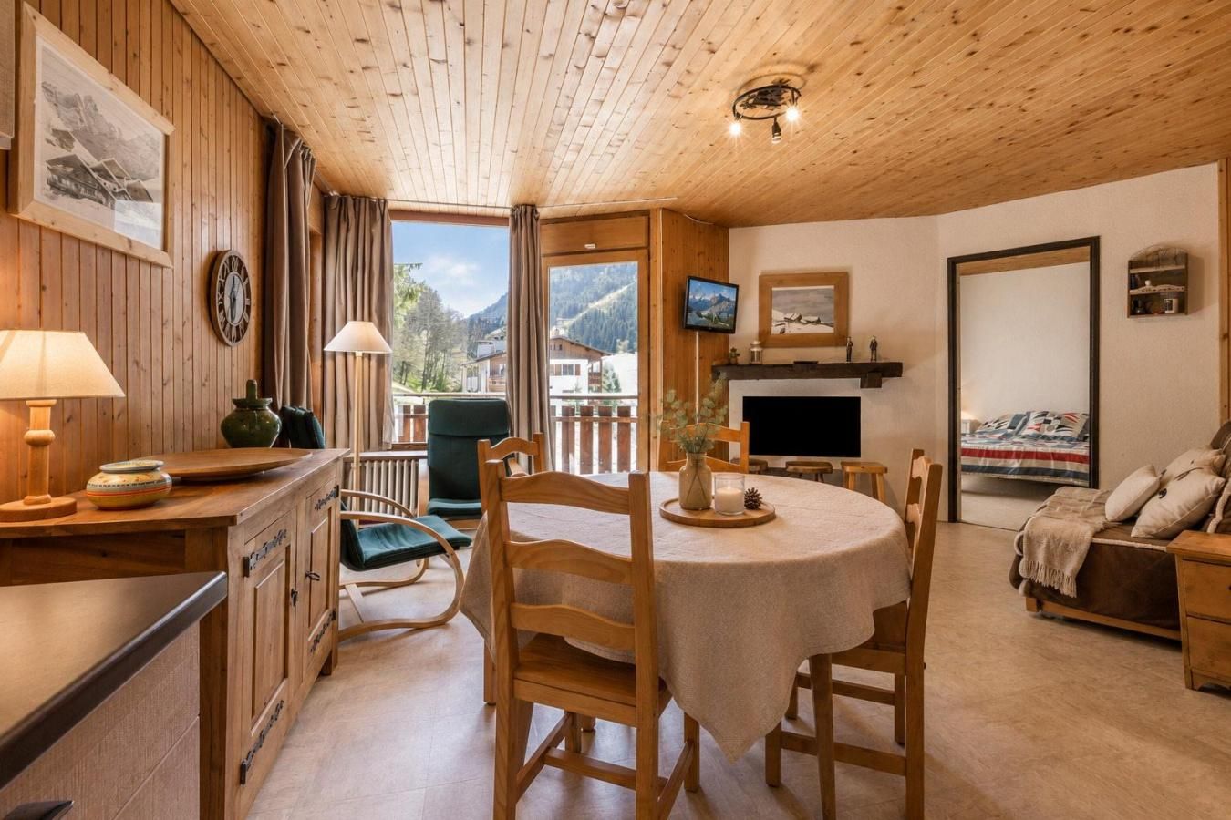 A cozy room with wooden walls, a dining table, chairs, a TV, and a bed.