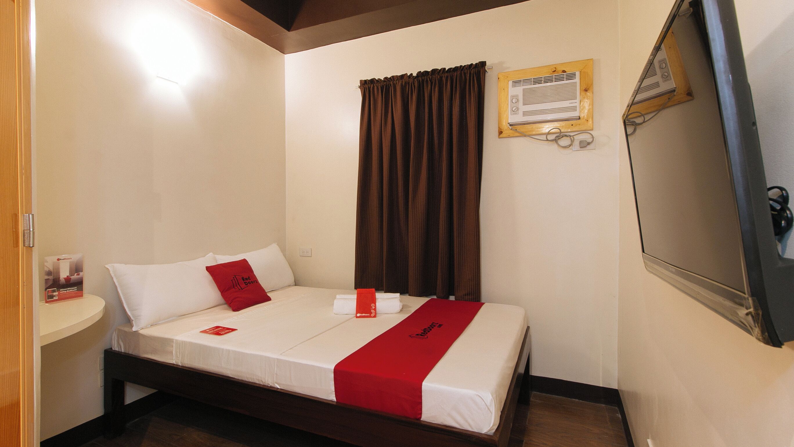 Habitación de hotel con cama, mesita de noche, espejo, ventana con cortinas y aire acondicionado instalado en la pared.