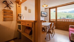 A cozy room with a wooden table, chairs, a TV, and a window with a view of the countryside.