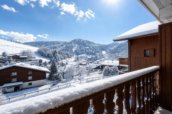 A snow-covered mountain village with wooden buildings and a balcony overlooking the snowy landscape.