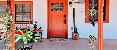 A red door with a welcome mat, potted plants, and a bench outside a building.
