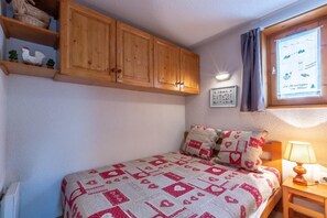 A bedroom with a bed, wooden cabinets, a window with curtains, and a wall-mounted lamp. - 250m from shops, 2nd floor, view resort/mountain, balcony, tv, ski locker, 26m², La Clusaz (La Clusaz)
