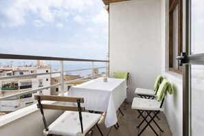Un balcón con mesa y sillas, vista a edificios y una ventana con una toalla.