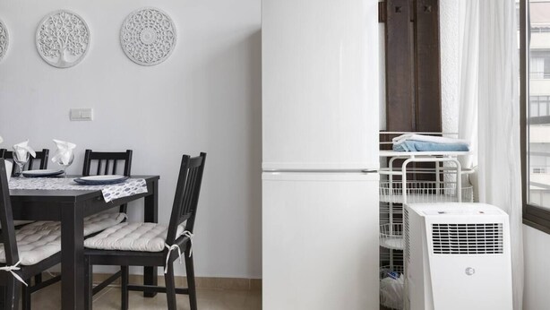Une cuisine compacte avec un réfrigérateur blanc, une table à manger avec des chaises et une fenêtre donnant sur la ville.