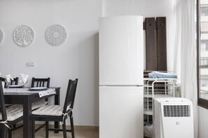 A compact kitchen with a white refrigerator, a dining table with chairs, and a window with a view of the city.