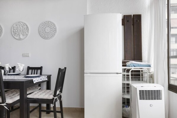 Cocina compacta con un refrigerador blanco, una mesa de comedor con sillas y un ventanal con vista a la ciudad.