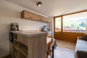 A compact kitchen with a coffee machine, wooden cabinets, and a dining area with a table and chairs.