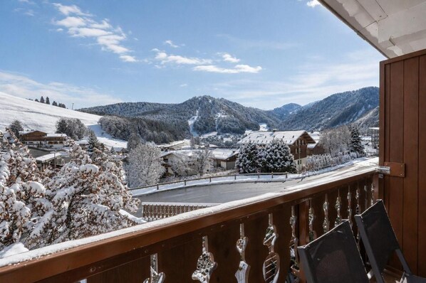A snowy mountain landscape with a wooden balcony overlooking a village.