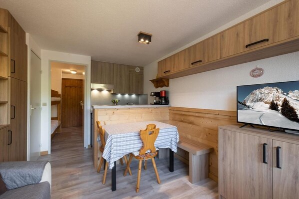 A compact kitchen with wooden cabinets, a dining table with a checkered tablecloth, and a television on a wooden cabinet.