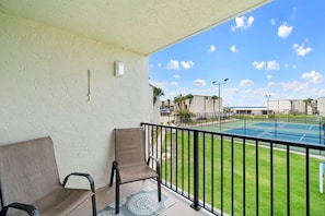 A balcony with two chairs, a tennis court, and a clear sky. - 2BR Condo Sleeps 6 • Pool & Steps to Beach (Panama City Beach)