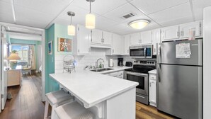 A modern kitchen with white cabinetry, stainless steel appliances, and pendant lighting. - 2BR Condo Sleeps 6 • Pool & Steps to Beach (Panama City Beach)