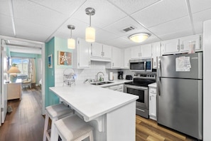 A modern kitchen with white cabinets, stainless steel appliances, and pendant lighting. - 2BR Condo Sleeps 6 • Pool & Steps to Beach (Panama City Beach)