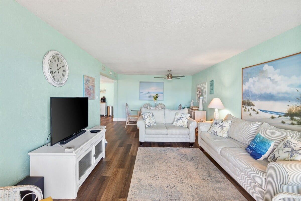 A living room with a television, two couches, a rug, and a painting of a beach.
