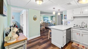 A modern kitchen with white cabinets, a central island, and a dining area with a table and chairs. - 2BR Condo Sleeps 6 • Pool & Steps to Beach (Panama City Beach)