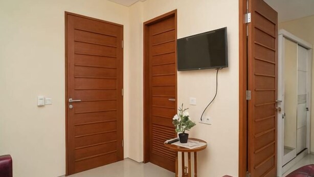 A hallway with wooden doors, a mounted TV, a small table with a plant, and red chairs. - RedDoorz near ITDC Nusa Dua (Bali)