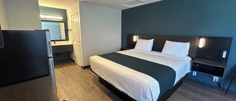 A hotel room with a bed, a desk, a chair, a TV, and a bathroom.