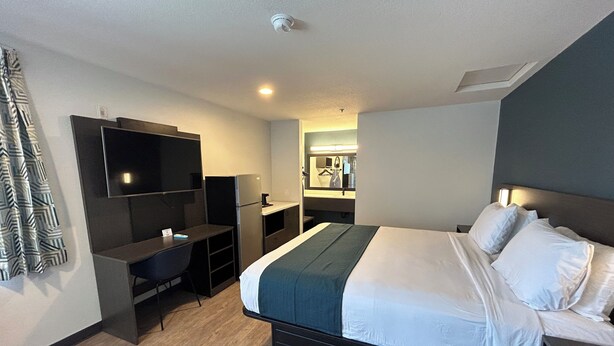 A hotel room with a bed, a desk, a TV, a mirror, and a kitchenette. - Studio 6 Lake Elsinore, Ca (Lake Elsinore)