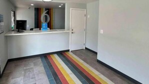A hallway with a striped floor, a reception desk, a door, and a monitor. - Studio 6 Lake Elsinore, Ca (Lake Elsinore)