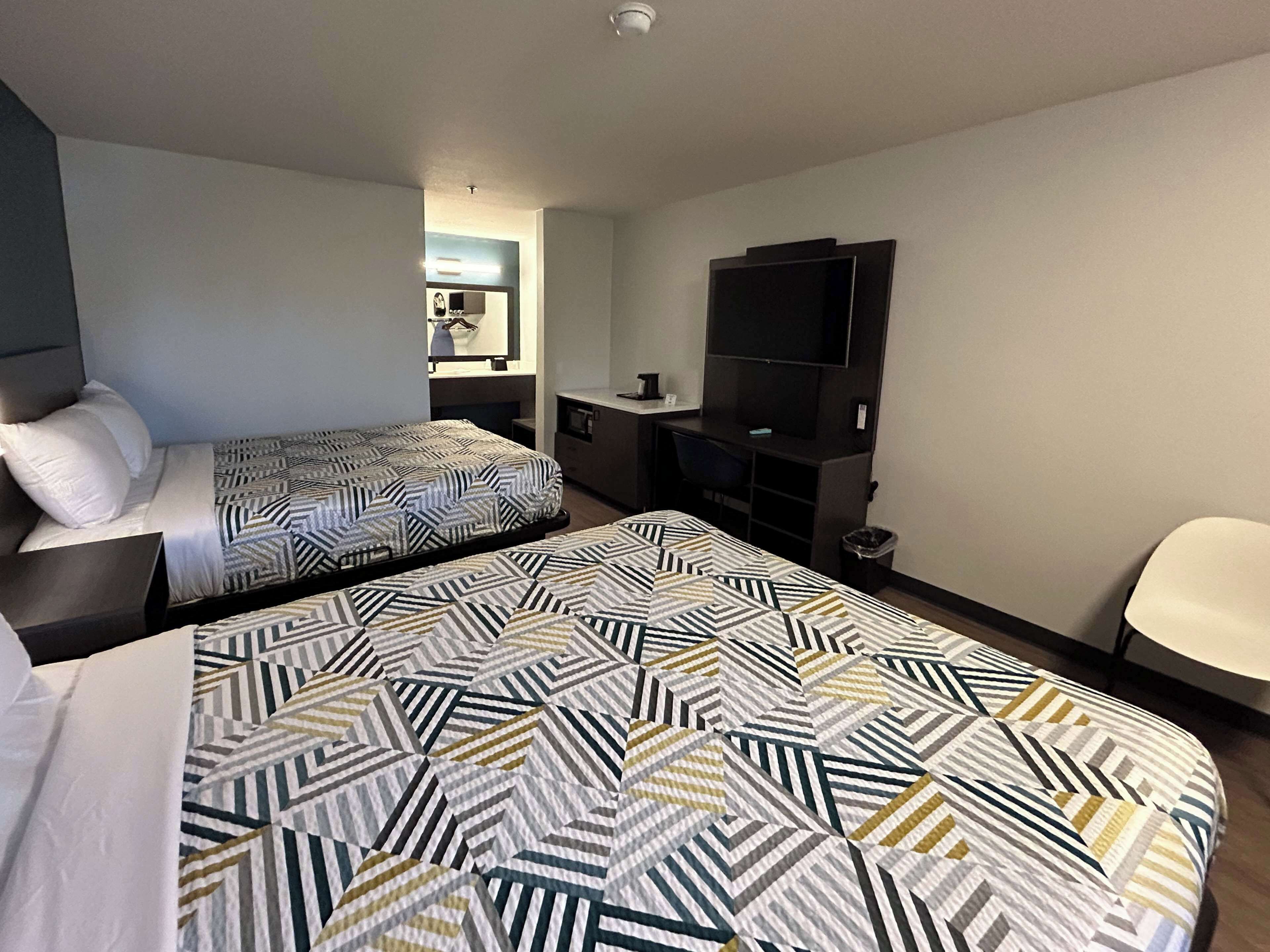 A hotel room with two beds, a TV, a desk, and a chair.