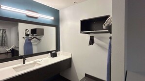 A modern bathroom with a large mirror, a white sink, and a black shelf with toiletries. - Studio 6 Lake Elsinore, Ca (Lake Elsinore)