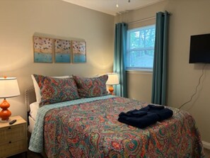 Un dormitorio con cama, dos mesitas de noche, una ventana con cortinas y decoración en la pared.