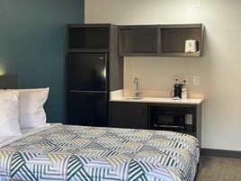 A compact hotel room with a bed, a kitchenette, and a microwave.