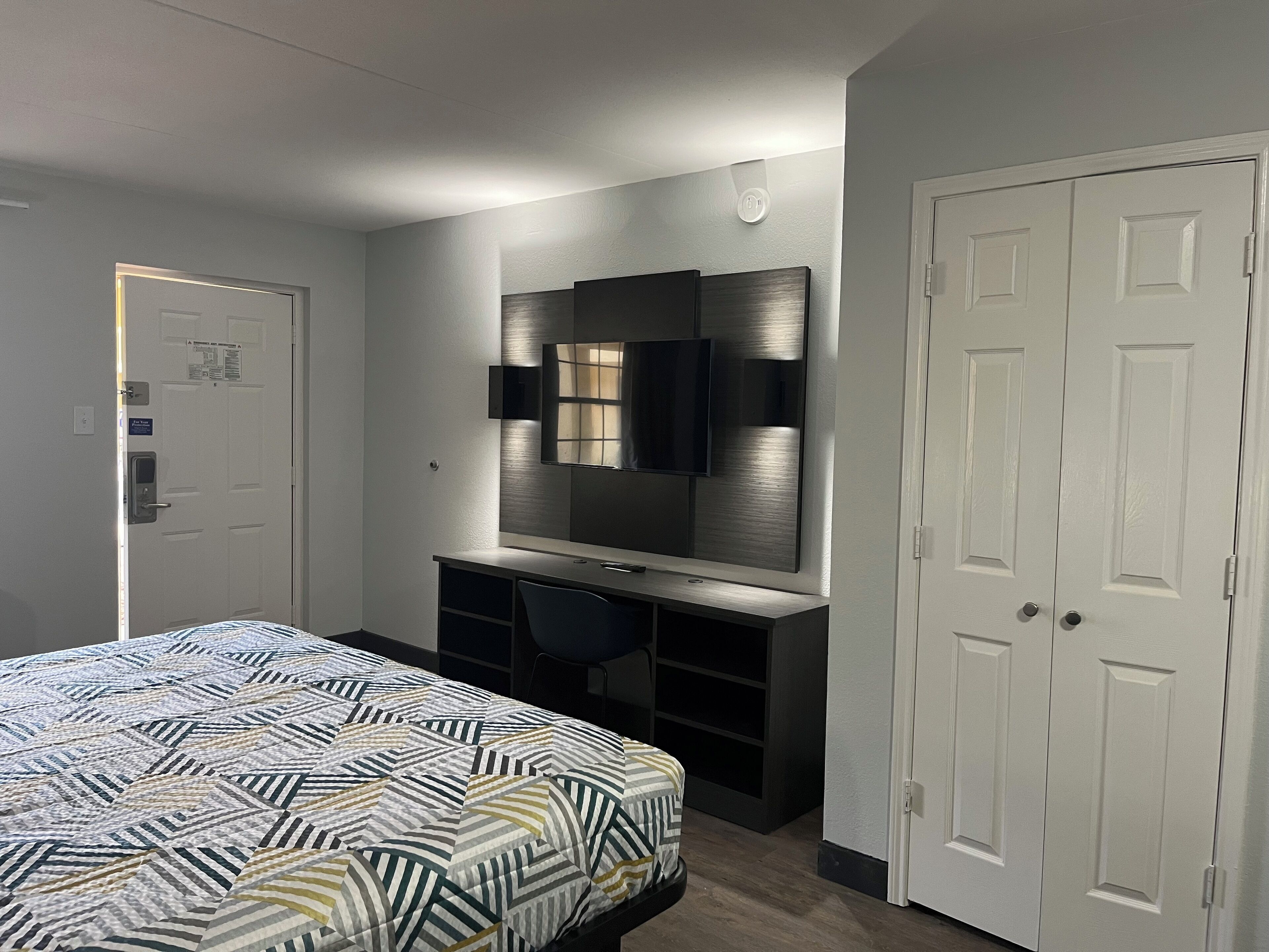 Een slaapkamer met een bed, een bureau, een stoel, een televisie en een kledingkast.