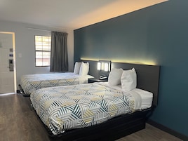 A hotel room with two beds, a nightstand, a phone, and a window with curtains.