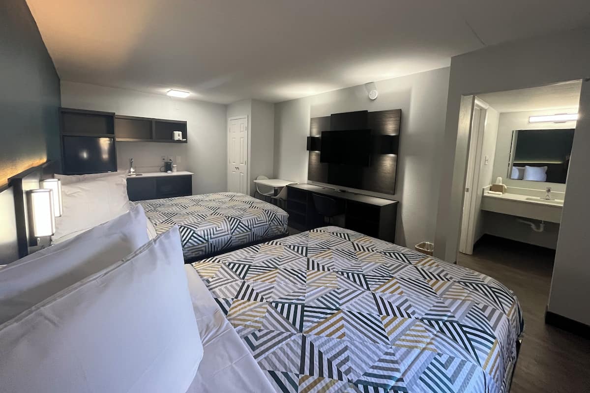 A hotel room with two beds, a desk, a TV, and a bathroom.