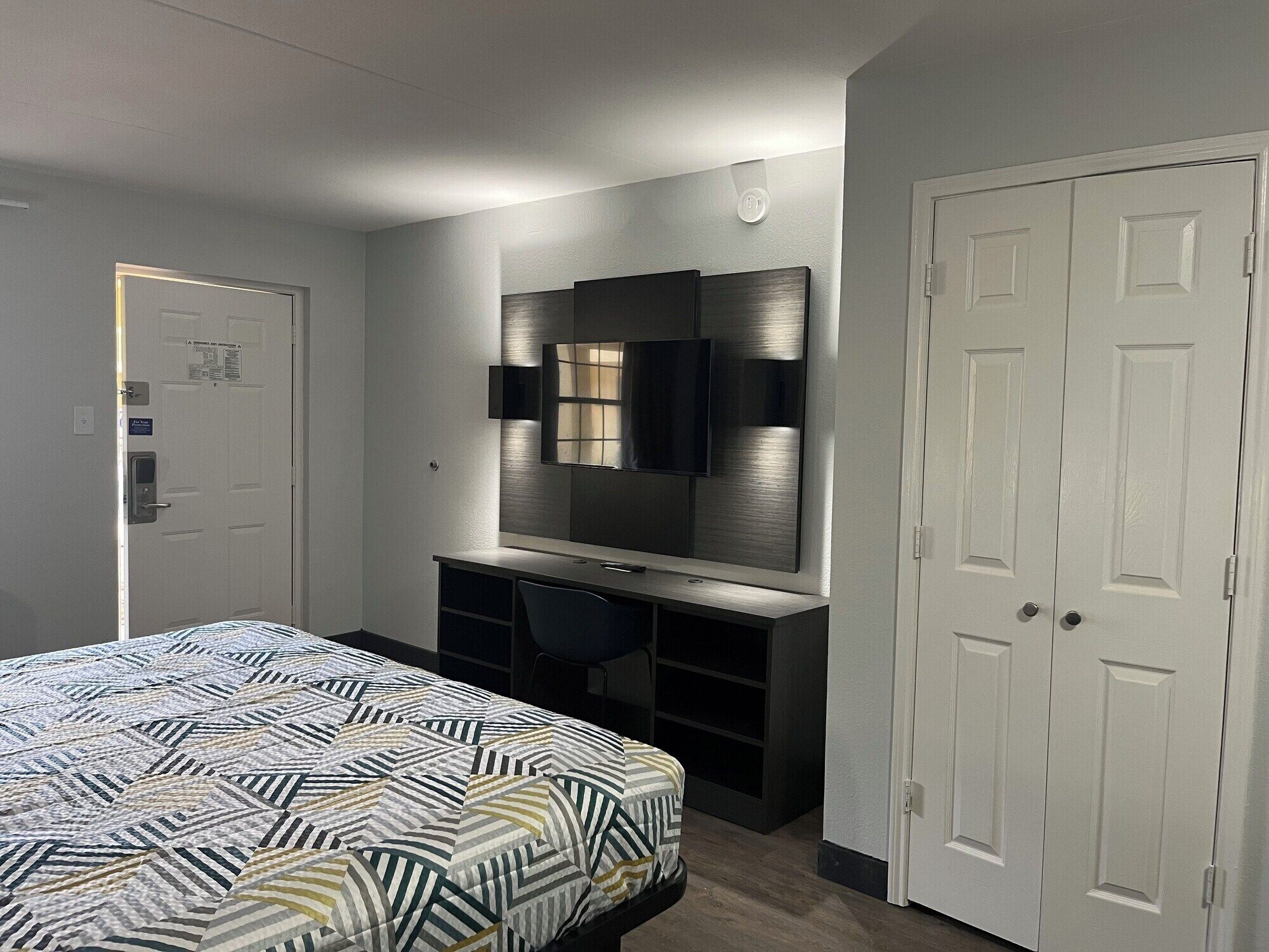 Une chambre d’hôtel comprenant un lit, un bureau avec une chaise, un grand miroir et une armoire.
