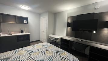 Ein Hotelzimmer mit Bett, Schreibtisch, Stuhl, Fernseher, Waschbecken und Kleiderschrank.