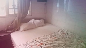 Una cama individual con edredón estampado, una ventana con cortinas y un aire acondicionado de pared.