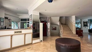 A hotel reception area with a marble floor, a reception desk labeled "RECEPTION," a staircase, and a seating area. - Hotel Albora (Kusadasi)