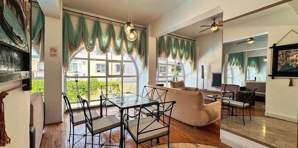 A spacious living area with a glass dining table, a sofa, and a ceiling fan. - Hotel Albora (Kusadasi)
