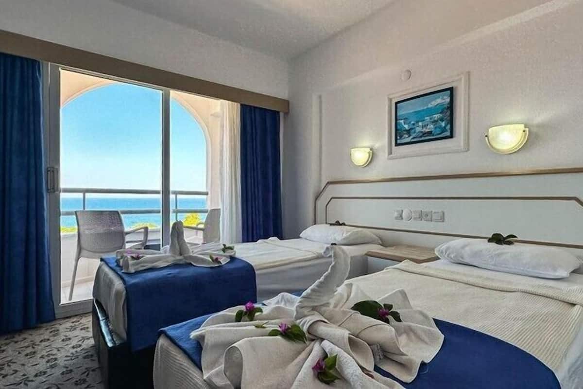 Une chambre d’hôtel avec deux lits, un balcon donnant sur la mer et un tableau encadré au mur.