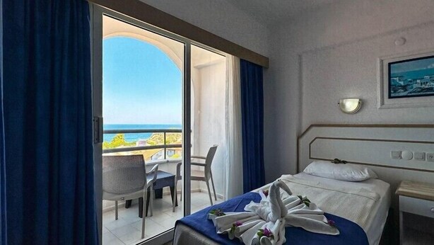 A hotel room with a bed, a desk, a chair, and a view of the sea. - Hotel Albora (Kusadasi)